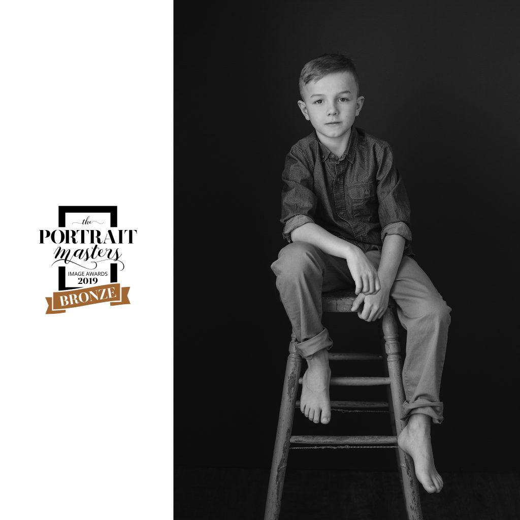 Black and white portrait of a boy seated on a stool.  Bronze award in children's portraiture. "Chase"