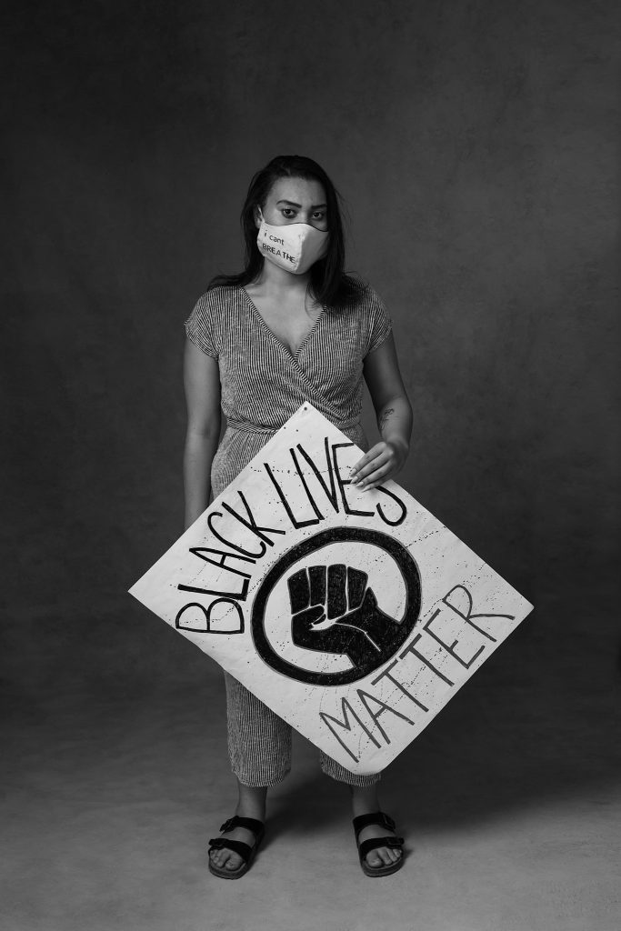 Black and white portrait of woman wearing mask and holding Black Lives Matter sign