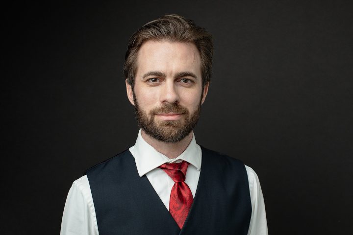 Men's headshot with vest and tie, black background