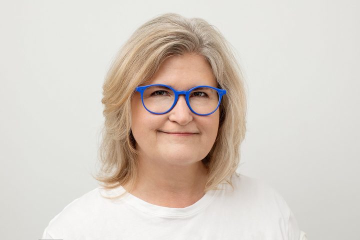 Headshot of woman wearing blue glasses, white t-shirt on white background