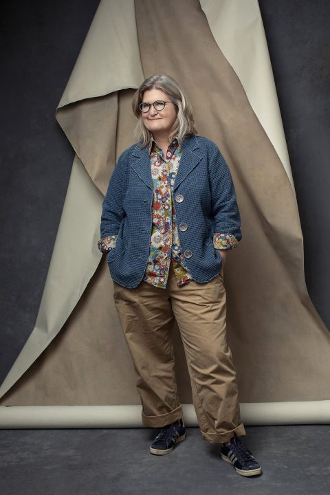 Evelyn, standing with hands in pockets, in front of a partially hung backdrop