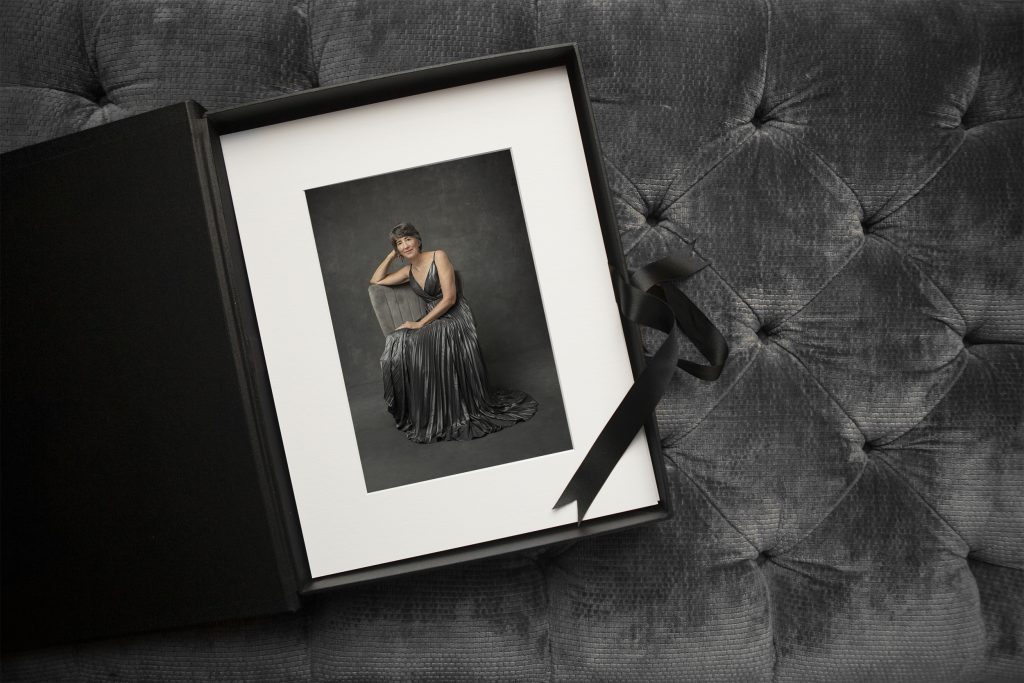 A folio box with matted prints on a gray velvet ottoman