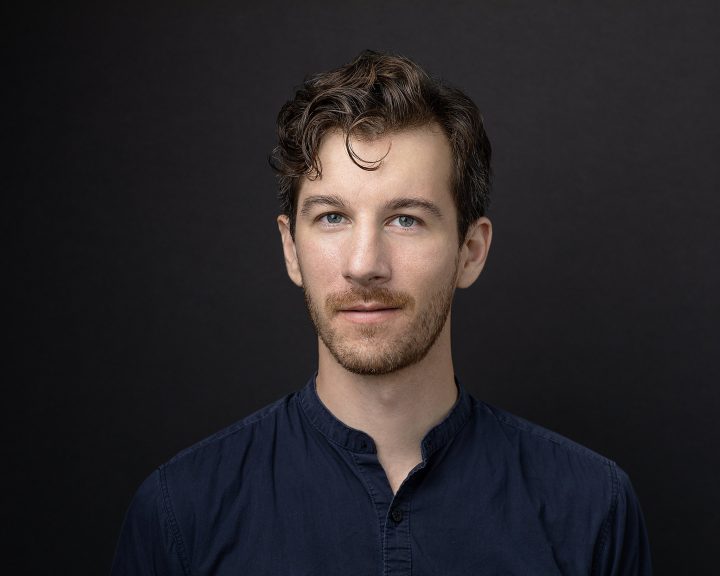 Headshot of cellist Alex Ellsworth in front of black background