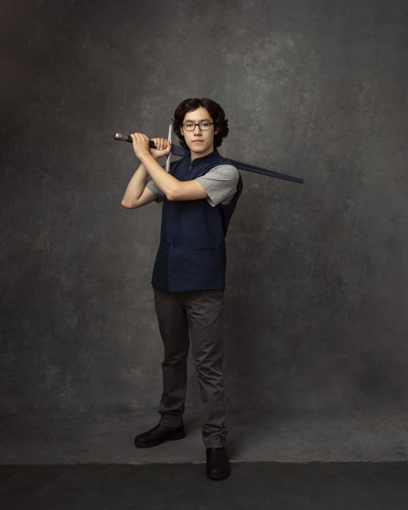 A portrait of a 16-year-old boy,  wearing a blue waistcoat, holding a practice sword