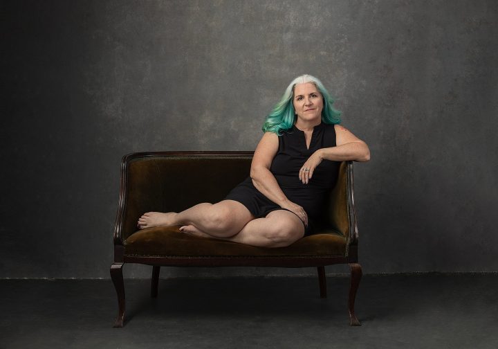 Portrait of Kim wearing a black dress, reclining on an antique velvet sofa