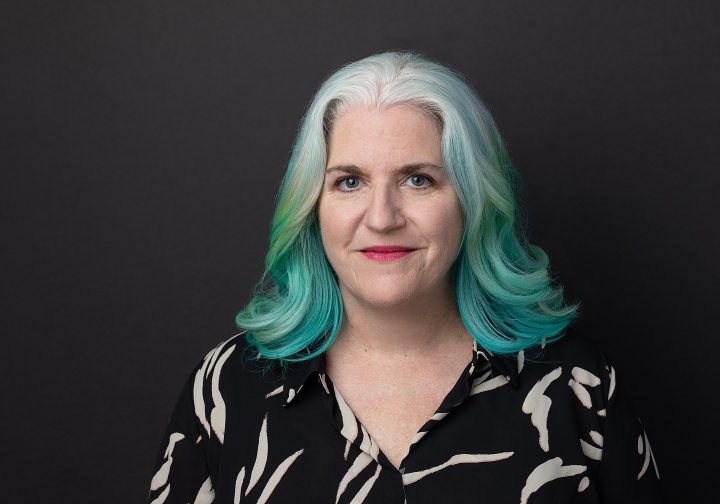 Headshot of Kim with blue hair and a black background for Extraordinary: the over 50 Revolution