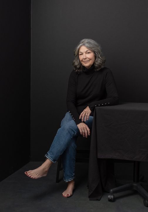 Portrait of Deb, seated, with bare feet, wearing a black turtleneck
