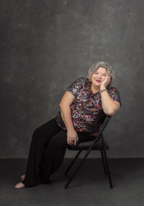 Portrait of Maria seated, wearing sparkly blouse for The Over 50 Revolution