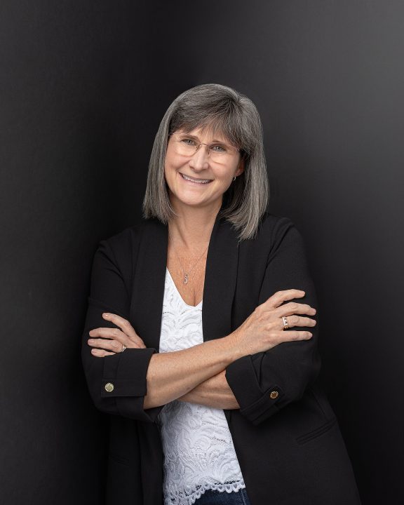 A branding portrait for Physical Therapist Melinda Johnston. She is leaning against a black background