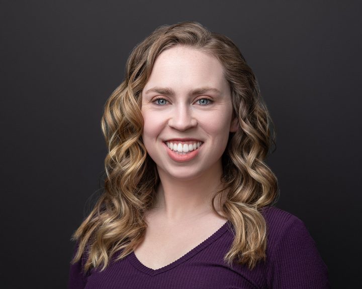 A headshot for Kenzie's five year update - She is smiling with black background