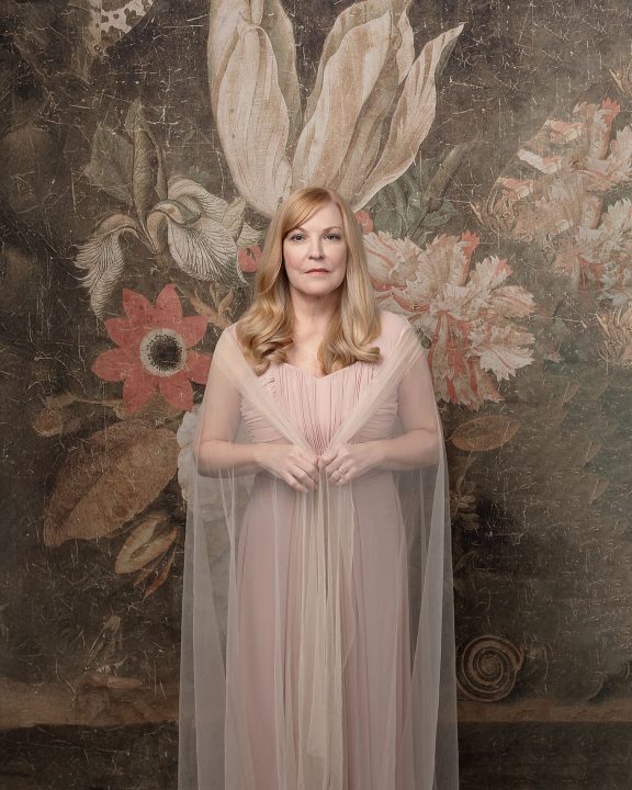 A portrait of Susan in front of an antique floral backdrop