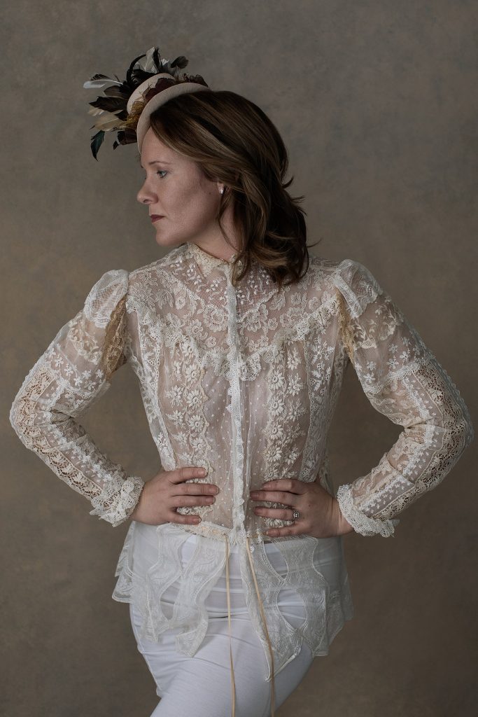 Neutral toned profile portrait of Rebecca in antique lace top and little hat with feathers