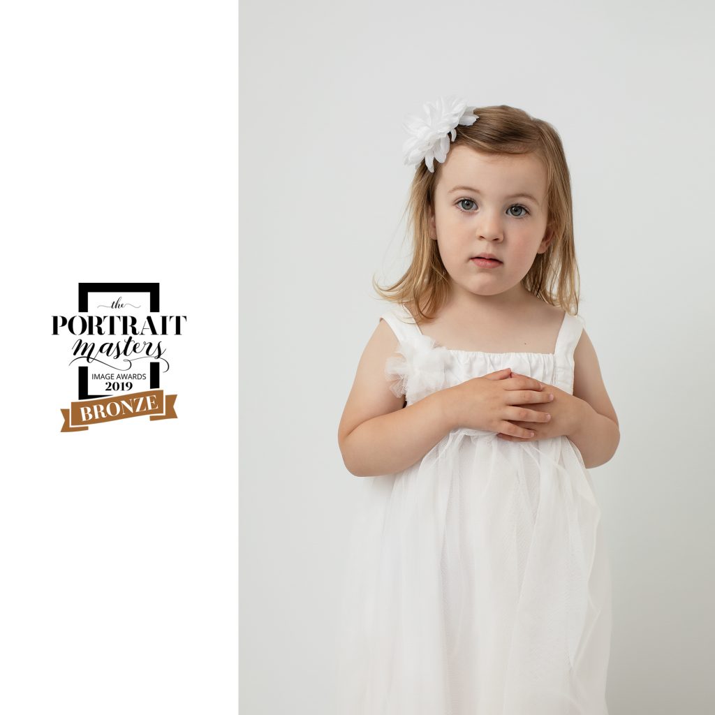 Piper, portrait of young girl in white dress with white background. Bronze award in Children's Portraiture