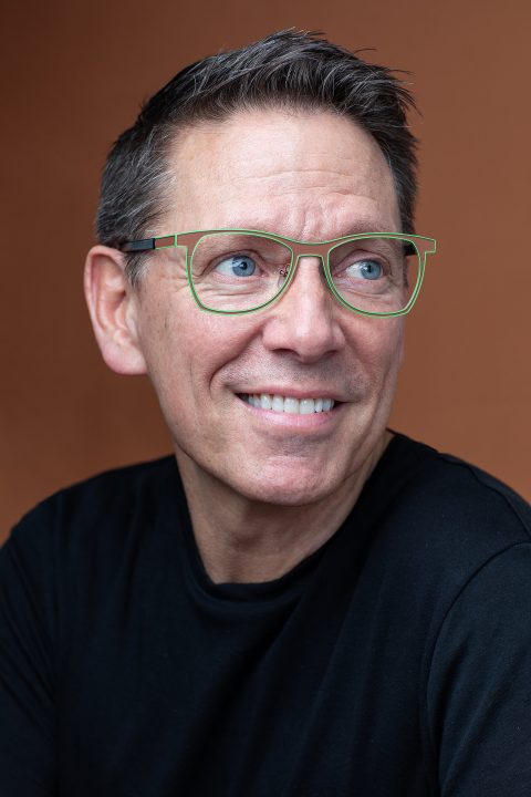 Portrait of Dan Perkins for Artisan Eyewear.  Wearing brown and green frames with brown background.