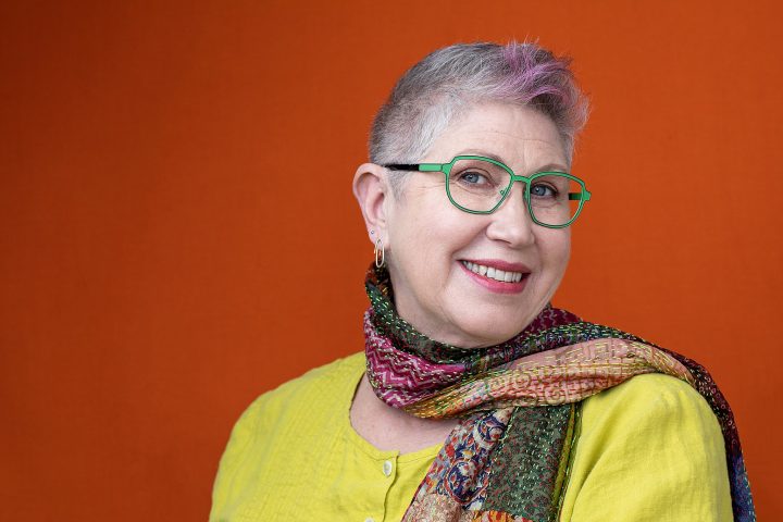 Portrait of Melissa McCarthy for Artisan Eyewear.  Wearing green eyeglass frames with an orange background.
