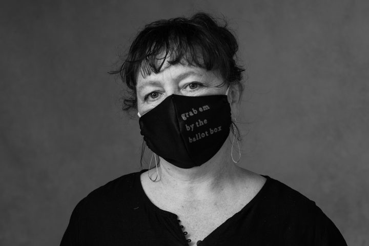 Black and white closeup portrait of a woman wearing a mask that reads "Grab 'em by the ballot box"