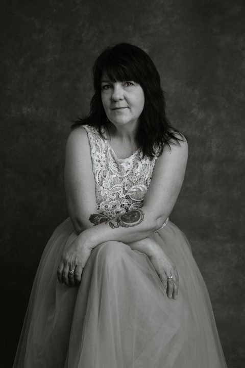 Black and white portrait of Kree wearing a tulle and lace dress, showing tattoos 