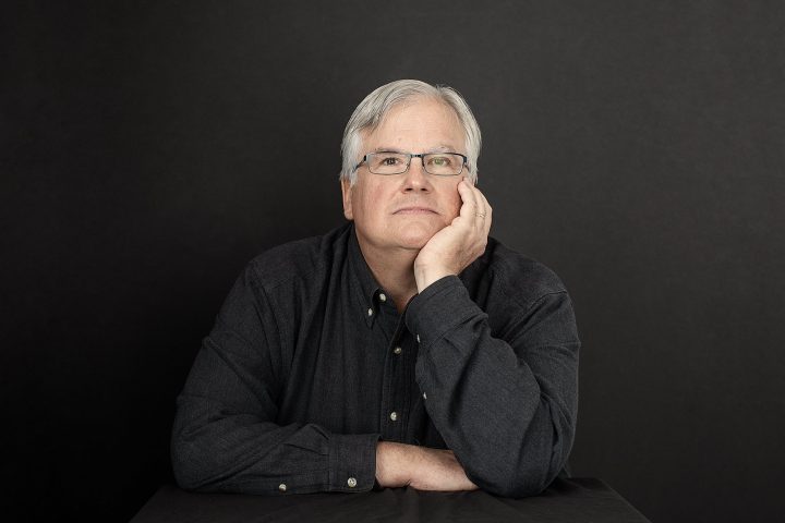 Pensive portrait of composer Jonathan Santore wearing a black shirt with a black background