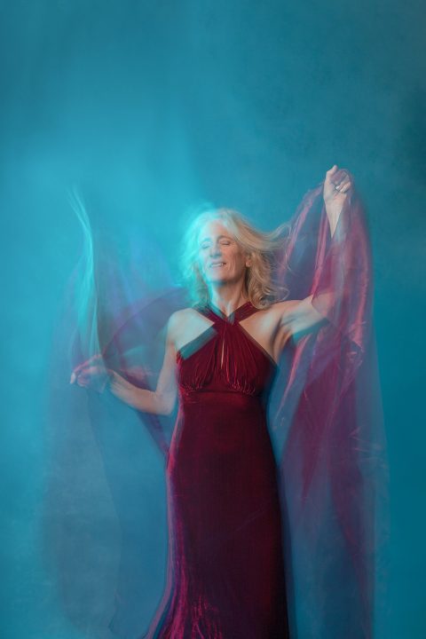 A portrait of Melinda in blue light wearing a red velvet dress with fabric and motion blur for an underwater effect.
