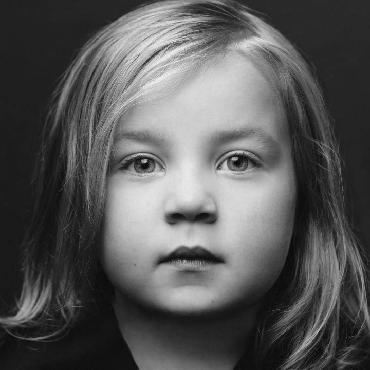 A square black and white closeup portrait of a young girl with a neutral expression.