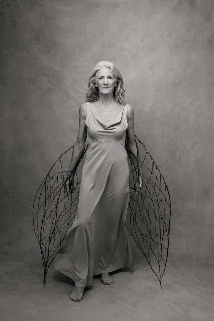 Black and white portrait of a confident woman in her 60s, with wings made of sticks