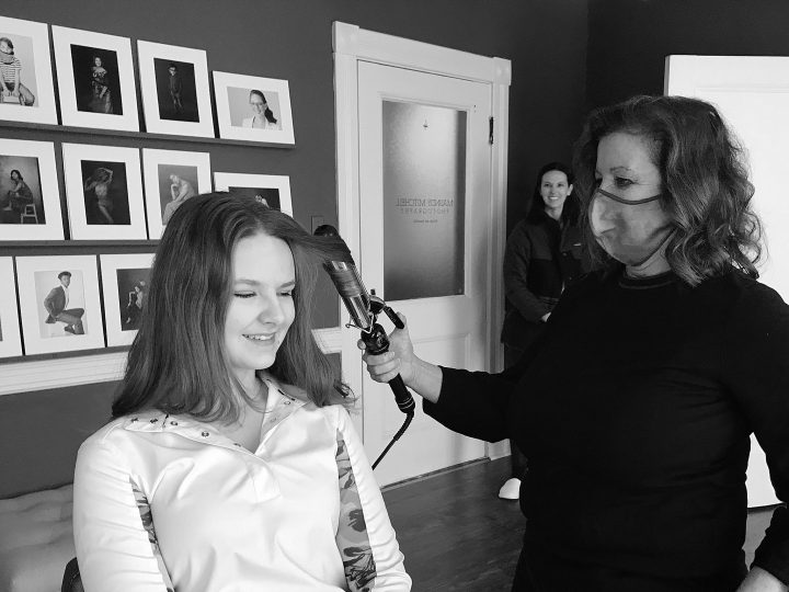 A black and white photo of Laurel enjoying professional hair and makeup styling as part of her senior photo session.