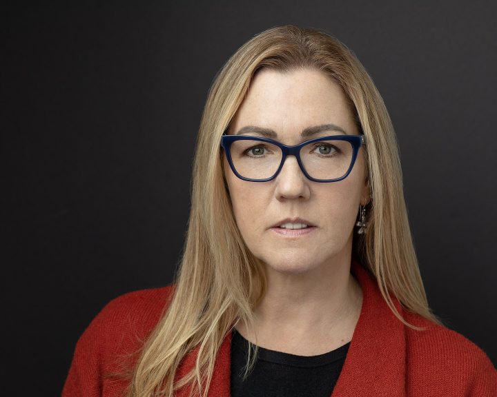 headshot of Boston area artist Amy Ford, wearing an orange sweater with a dark background