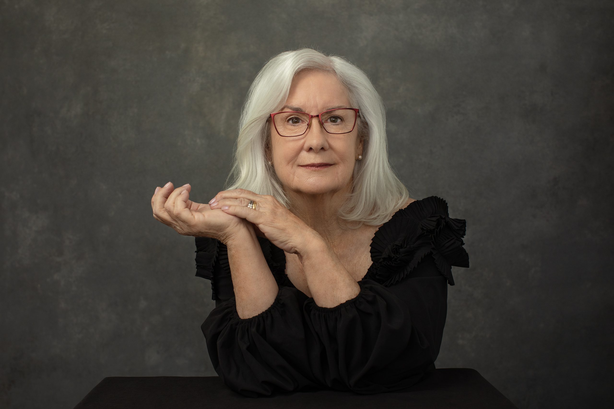 A stylish woman in her 70s, seated with her hands by her face