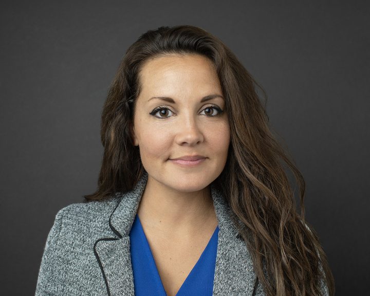 A business professional headshot of a woman wearing a jacket with a dark background