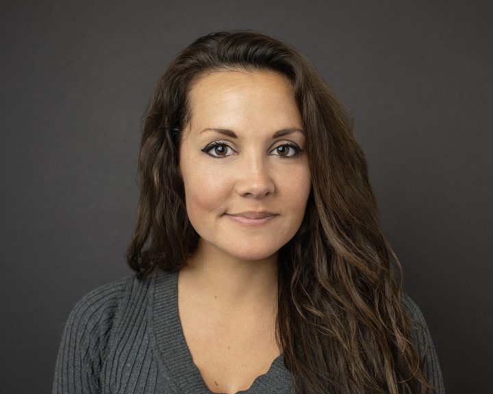 Business casual headshot of a woman wearing a gray sweater with a black background