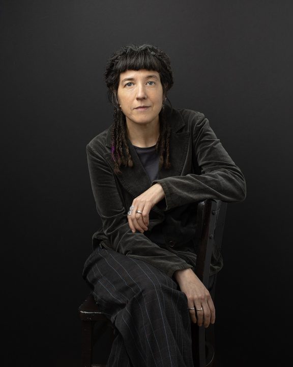 Portrait of theatre-maker and feminist writer Dr. Niki Tulk, seated with a black background
