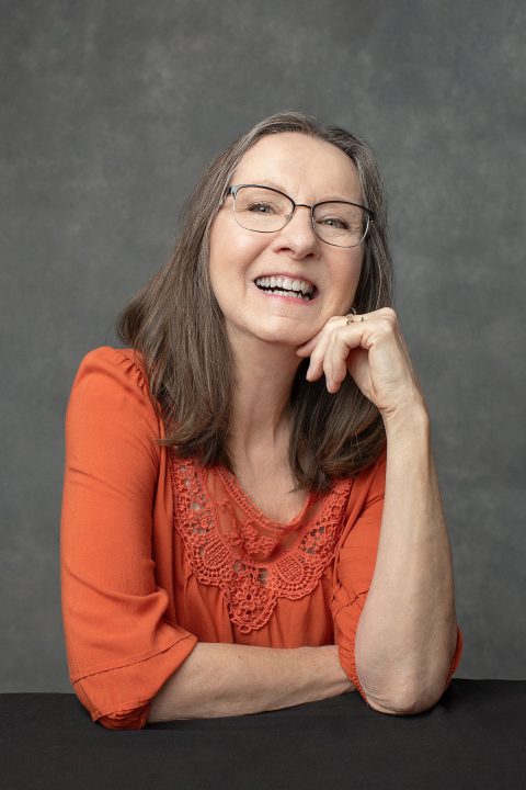 Casual portrait of Nancy wearing an orange top and glasses