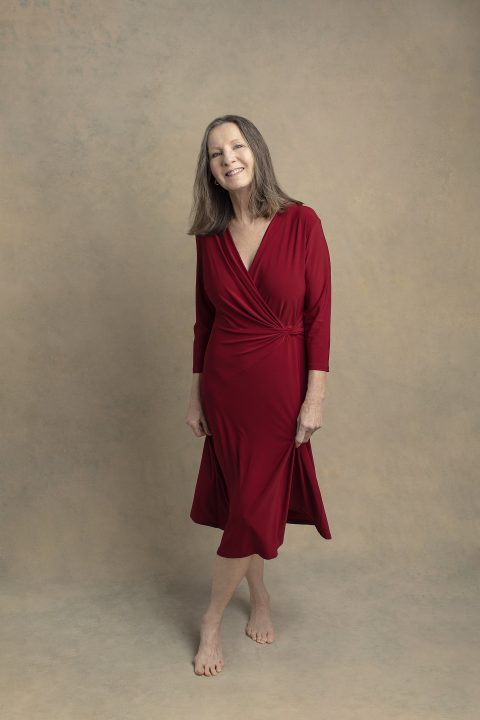 Portrait of Nancy wearing a red dress in front of a tan backdrop