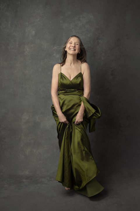 Portrait of Nancy, age 71, laughing, wearing an olive green satin gown
