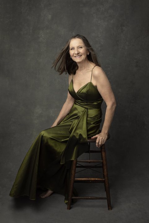 Portrait of Nancy, seated, wearing an olive green satin gown, smiling