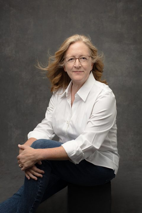 A casual portrait of a woman in her 60s wearing a white shirt and jeans