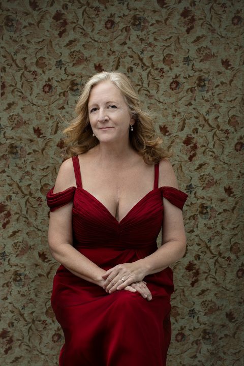 Portrait of a woman in a red silk dress in front of a wall with floral wallpaper