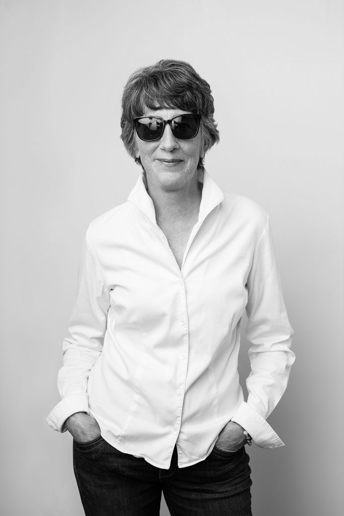 A portrait of a woman in her 60s wearing a white shirt and sunglasses