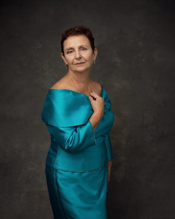An older woman with short hair wearing an elegant silk turquoise dress