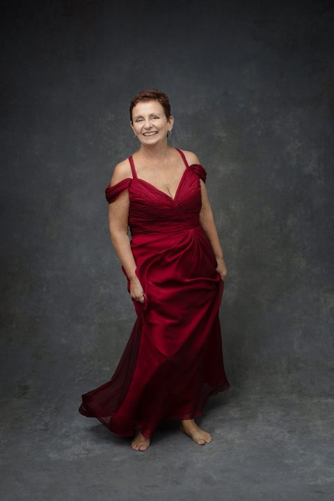 Portrait of a woman in her 60s wearing a long red silk gown, having fun