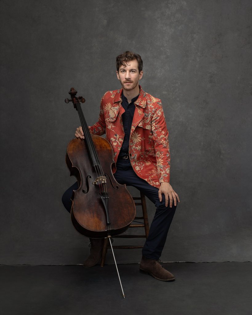 Portrait of cellist Alexander Ellsworth with cello, wearing floral jacket