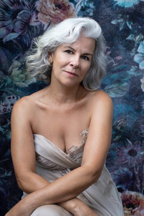 Portrait of a woman with white hair wearing a silk gown in front of a floral backdrop