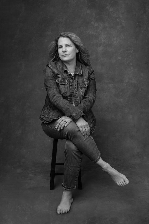 Casual black and white portrait of a woman seated on a stool