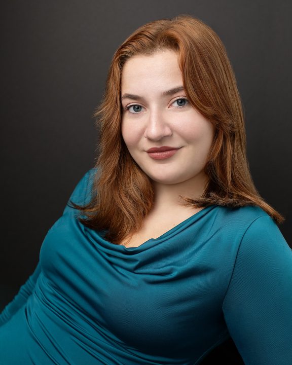 A portrait with a black background for an actor with red hair, who is wearing a teal shirt 