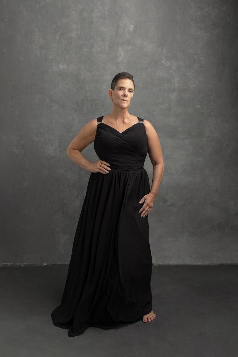 A woman in her 50s, after cancer, wearing a long black dress, with a confident expression and body language