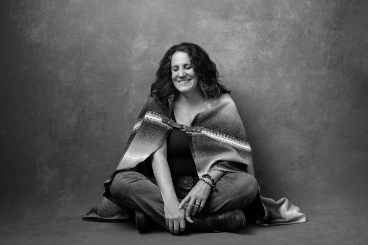 A photo for the Over 50 Revolution: a black and white portrait of a woman sitting, wrapped in a blanket, and laughing with her eyes closed