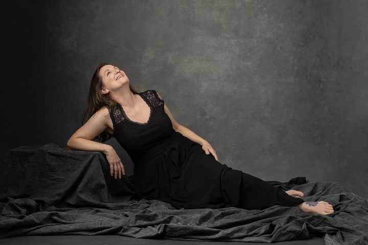 Studio portrait of a woman over 50, reclining, laughing, wearing a black dress