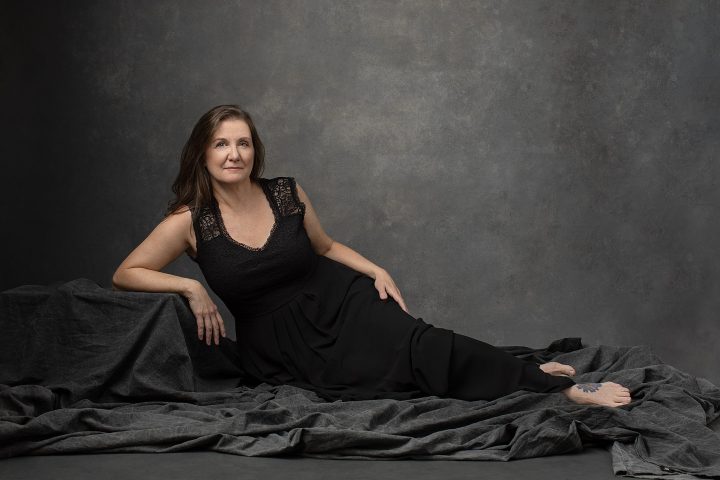 Studio portrait of a woman over 50 reclining, wearing a black dress