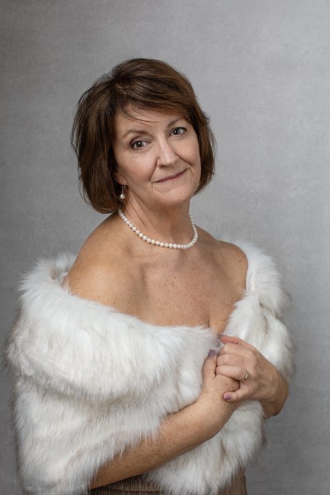 Susan, for Unforgettable: the Over 50 Revolution, wrapped in faux fur stole, wearing pearls