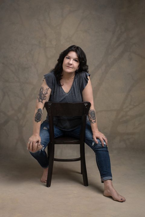 Portrait of Kree, sitting backward in a chair, with shadows of trees behind her